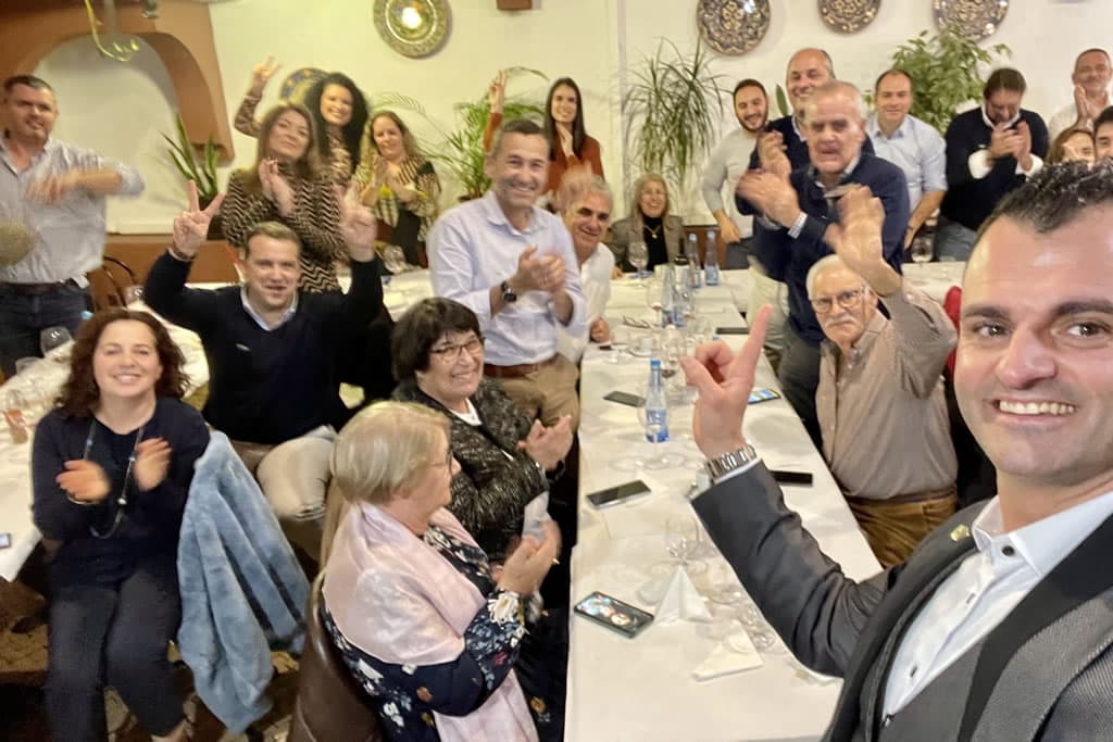Convidados sentados a uma mesa comprida de restaurante, a aplaudir, com o Nuno Rodrigues em primeiro plano