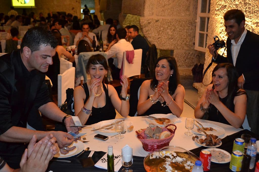 Nuno Rodrigues a fazer magia à mesa durante um jantar, com as convidadas a rir e a aplaudir