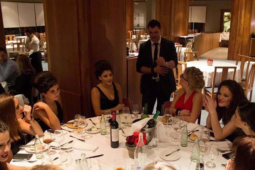 Nuno Rodrigues de pé junto a uma mesa de jantar, com as convidadas a rir